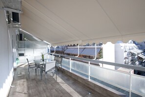 A balcony with a table and chairs, a potted plant, and a view of buildings in the background.