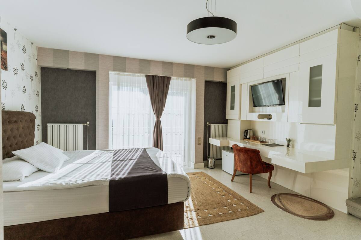 A modern bedroom with a large bed, a desk, a television, and a radiator.