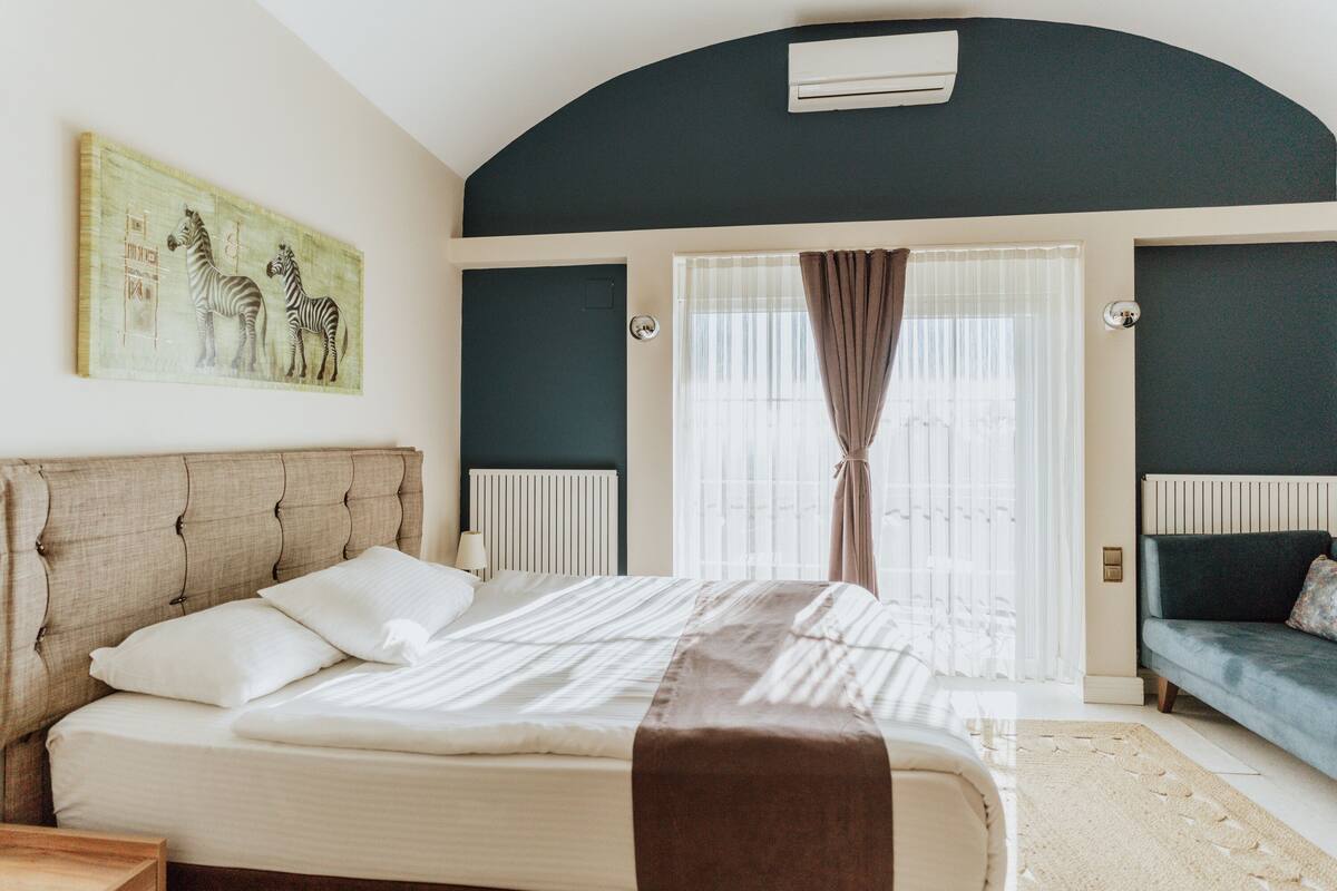 A bedroom with a large bed, a window with curtains, a radiator, and a wall-mounted air conditioner.