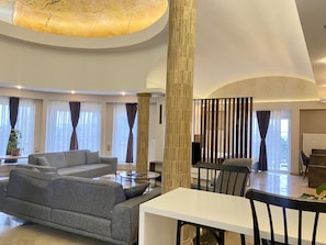Uma sala espaçosa com um sofá grande, uma mesa de jantar e um pilar alto.