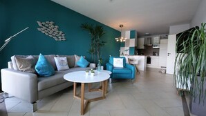 A modern living room with a white sofa, blue cushions, a round coffee table, and a kitchen in the background. - Fewo RheinDesign in Linz on the Romantic Middle Rhine with a beautiful river view (Linz am Rhein)