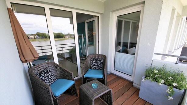 A balcony with wicker chairs and a small table, a sliding glass door, and a planter with flowers. - Fewo RheinDesign in Linz on the Romantic Middle Rhine with a beautiful river view (Linz am Rhein)