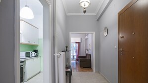 A narrow hallway with a kitchen on the left, a dining area with a table and chairs, and a living room with a sofa and a lamp on the right. - Two Bedroom Apartment at Koukaki (Athens)