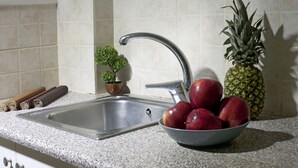 A kitchen with a stainless steel sink, a bowl of red apples, a pineapple, and a small potted plant. - Two Bedroom Apartment at Koukaki (Athens)