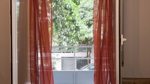 A view through a sliding glass door with red curtains, leading to a balcony with a metal railing and a car parked outside. - Two Bedroom Apartment at Koukaki (Athens)