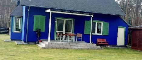 A blue house with a covered porch, a satellite dish, and a small outdoor seating area.