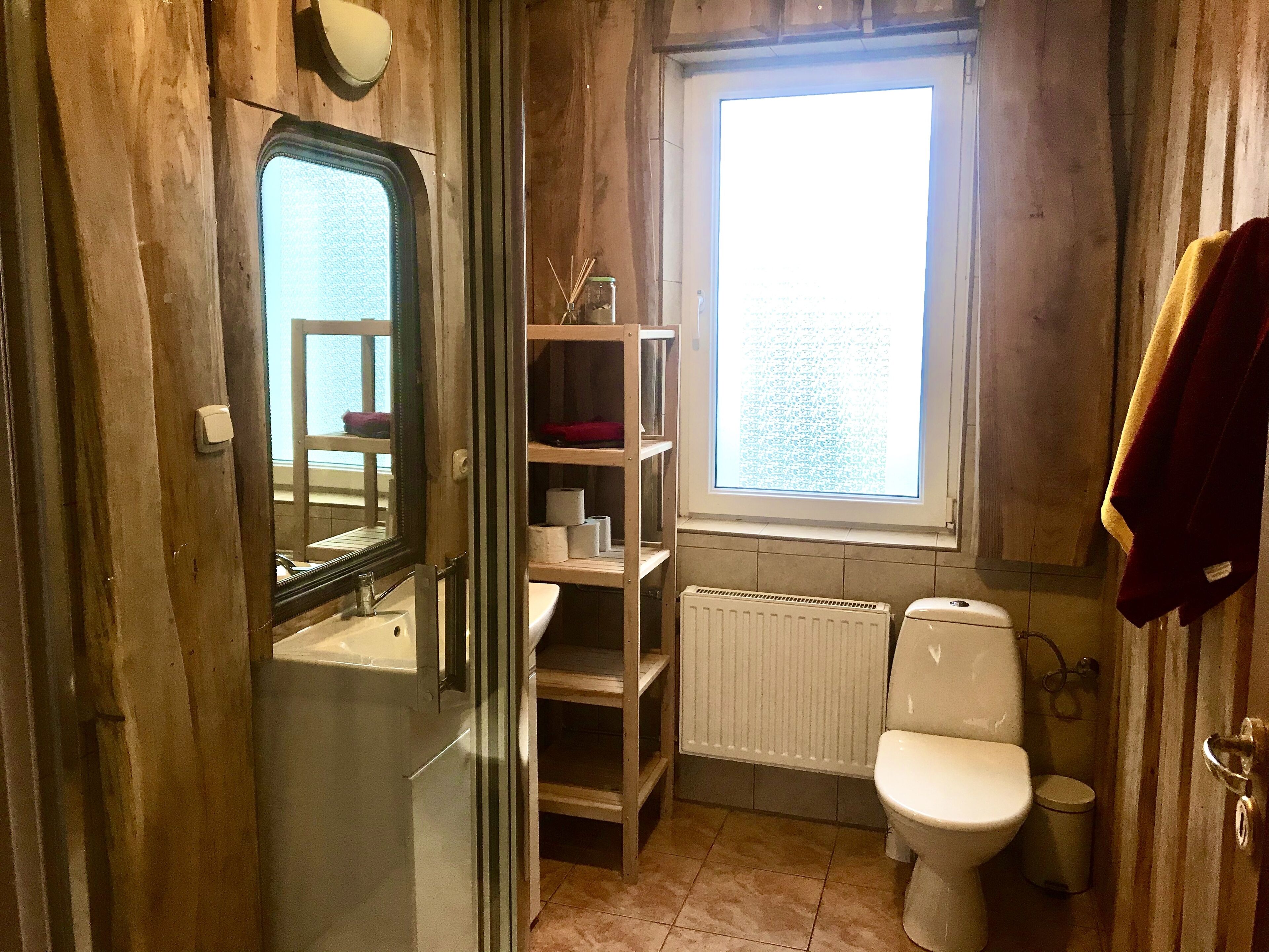 Ein Badezimmer mit Toilette, Heizkörper, Ablage für Toilettenartikel und einem Fenster.