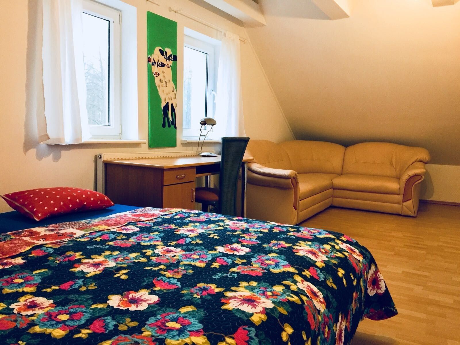 Et soveværelse med seng, skrivebord, stol, sofa og et vindue.
