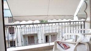 Ein Balkon mit weißen Plastikstühlen und einer Zeitschrift, mit Blick auf ein Gebäude mit Balkonen und Geländern.