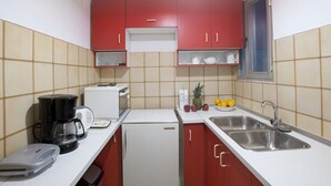 Eine kompakte Küche mit roten Schränken, einer weißen Arbeitsplatte, einer Kaffeemaschine, einem Toaster, einem Kühlschrank und einem Spülbecken.