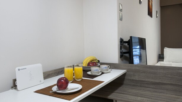 Ein Hotelzimmer mit Frühstücksbereitstellung, darunter ein weißer Tisch, eine Obstschale, eine Obstplatte, zwei Gläser Orangensaft und eine Kaffeestation.