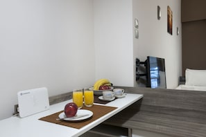 A hotel room with a breakfast setup including a white table, a fruit bowl, a fruit plate, two glasses of orange juice, and a coffee setup. - Studio Next to Agios Nikolaos Church (Athens)