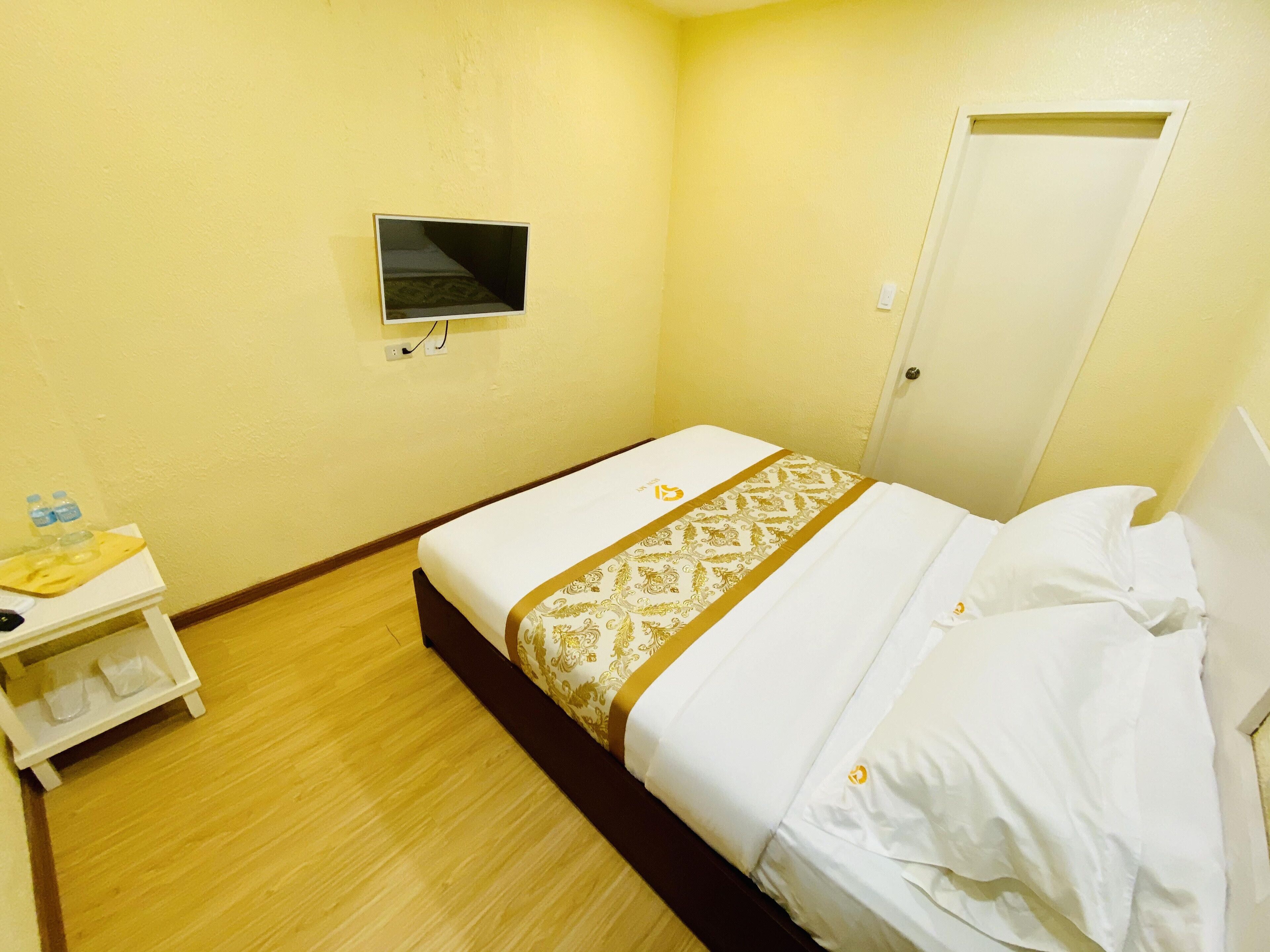 A hotel room with a bed, a small bedside table with a water bottle, and a TV mounted on the wall.