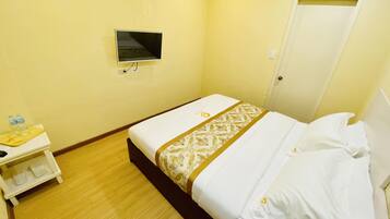 A hotel room with a bed, a small bedside table with a water bottle, and a TV mounted on the wall.