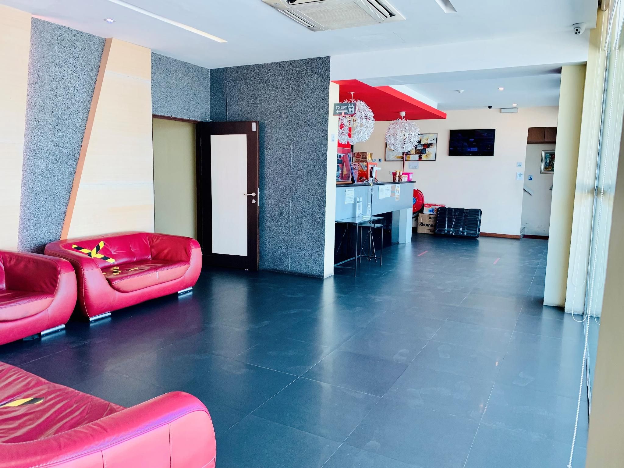A modern lobby with a reception desk, a red and white decorative ceiling, and a seating area with red sofas.