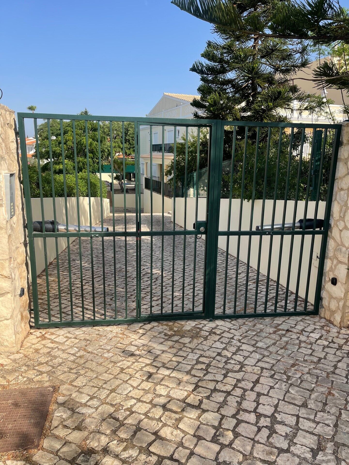A gated driveway leading to a building with a tiled roof and a stone wall.