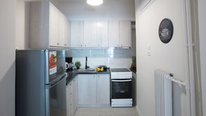 A compact kitchen with white cabinets, a stainless steel refrigerator, a built-in oven, and a coffee machine. - Zan Moreas A Simple & Minimal Apartment (Athens)