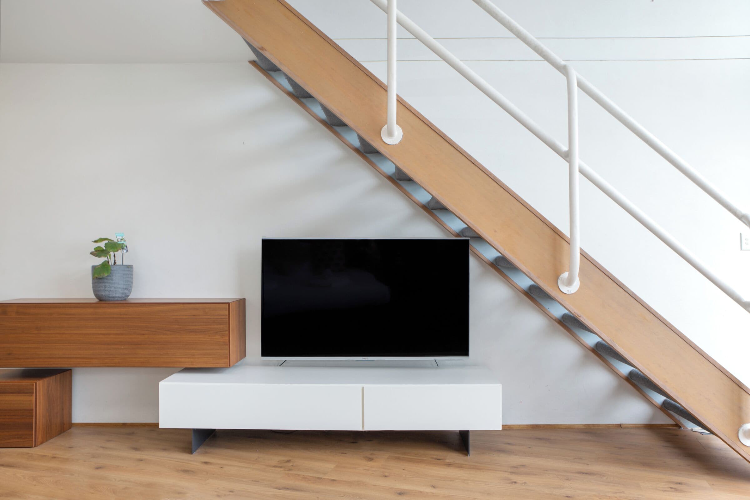 Een moderne woonkamer met een houten trap, een witte tv-meubel en een plant in pot.