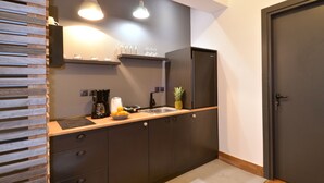 A modern kitchen with dark cabinetry, a wooden countertop, a coffee maker, a fruit bowl, and a refrigerator.