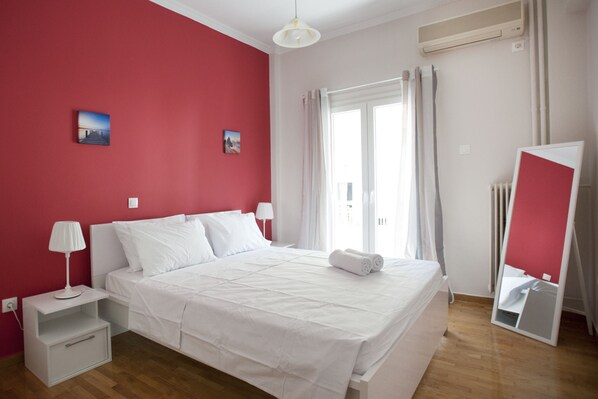 A hotel room with a bed, white nightstands, a mirror, and a window with curtains. - Pop art apartment at Koukaki (Athens)
