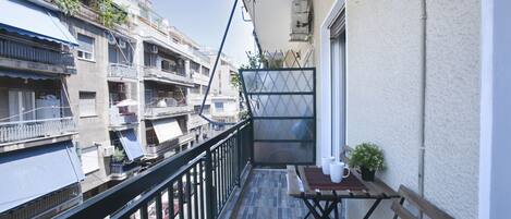 A balcony with a wooden table, a bench, and a potted plant.
