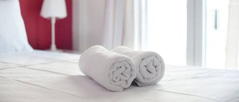 A neatly made bed with white linens and two rolled towels placed on it.