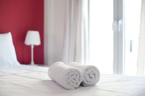 A neatly made bed with white linens and two rolled towels placed on it. - Pop art apartment at Koukaki (Athens)