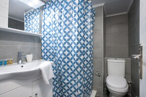 A bathroom with a white sink, a toilet, and a shower curtain with a geometric pattern. - Pop art apartment at Koukaki (Athens)