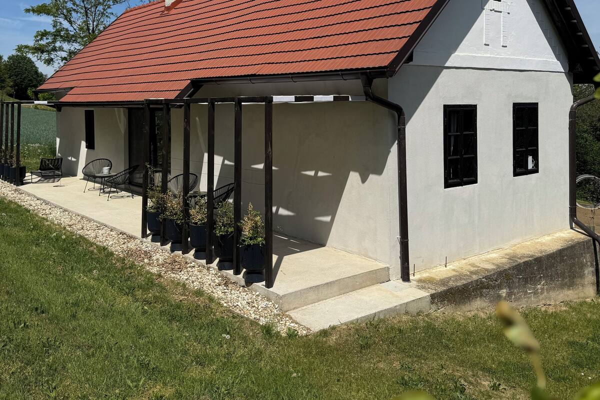 Une maison moderne avec un toit recouvert de tuiles rouges, une véranda et un petit jardin.