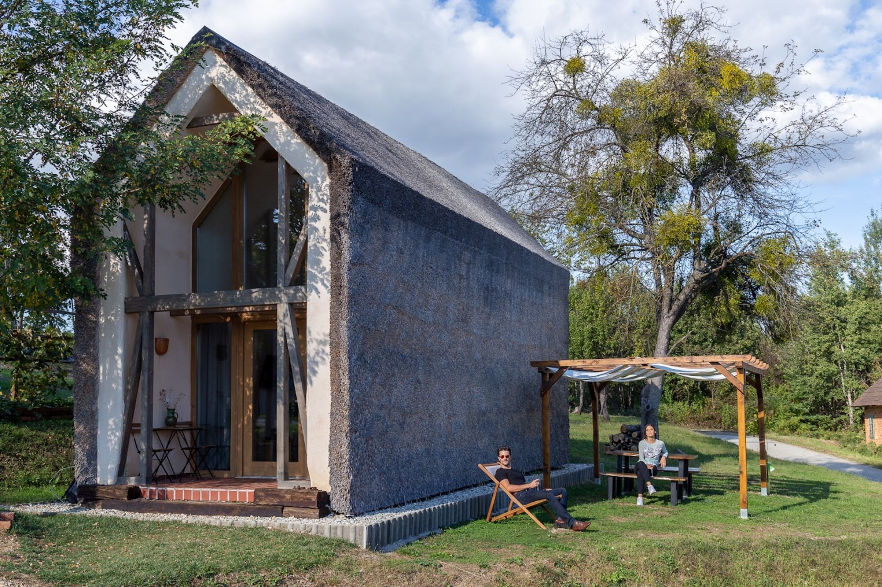 A small stone building with a sloped roof, a wooden pergola, and a picnic table.
