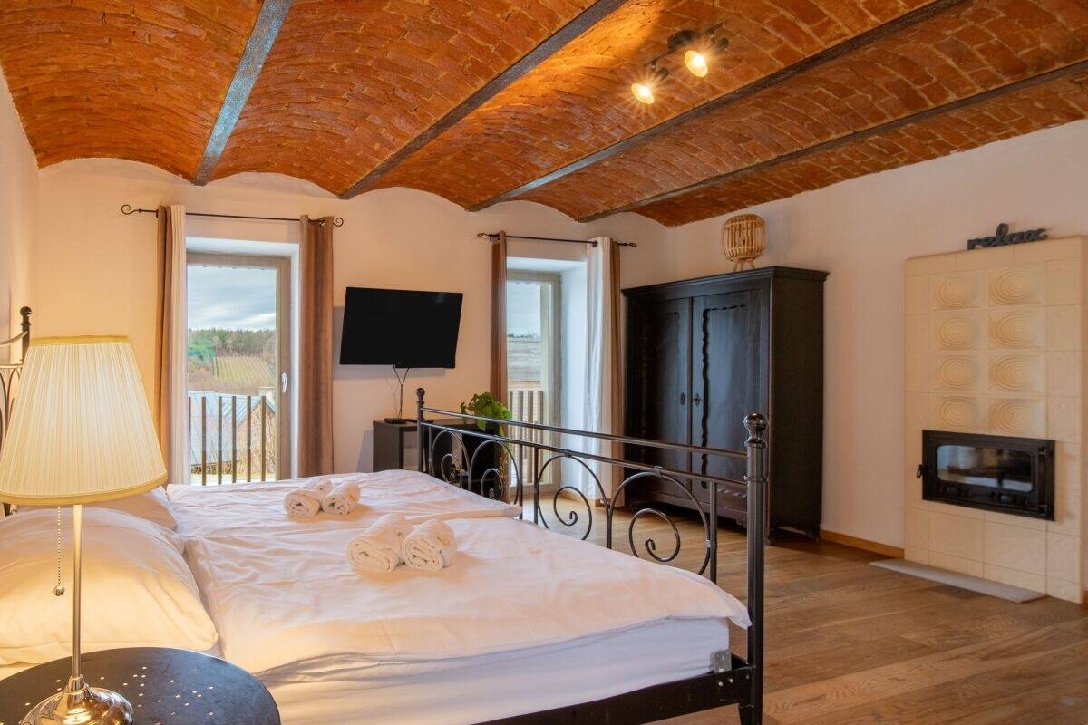 Une chambre avec un plafond en briques, un lit avec du linge de lit blanc, une lampe de chevet, une télévision, une armoire et une cheminée.