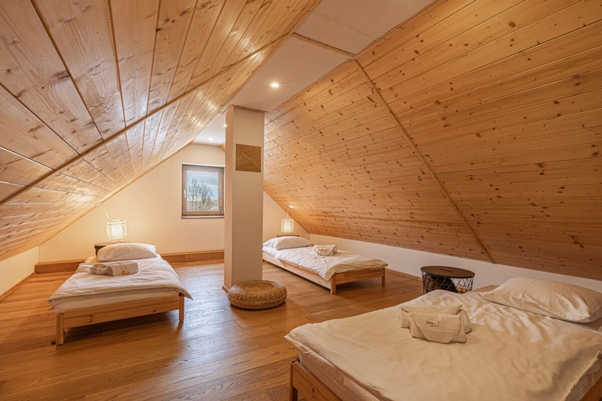 Une chambre confortable située dans les combles, avec des poutres en bois, deux lits, une petite table ronde et un panier.