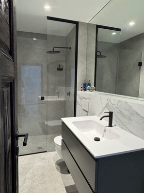 A modern bathroom with a glass-enclosed shower, a white sink, and a large mirror.