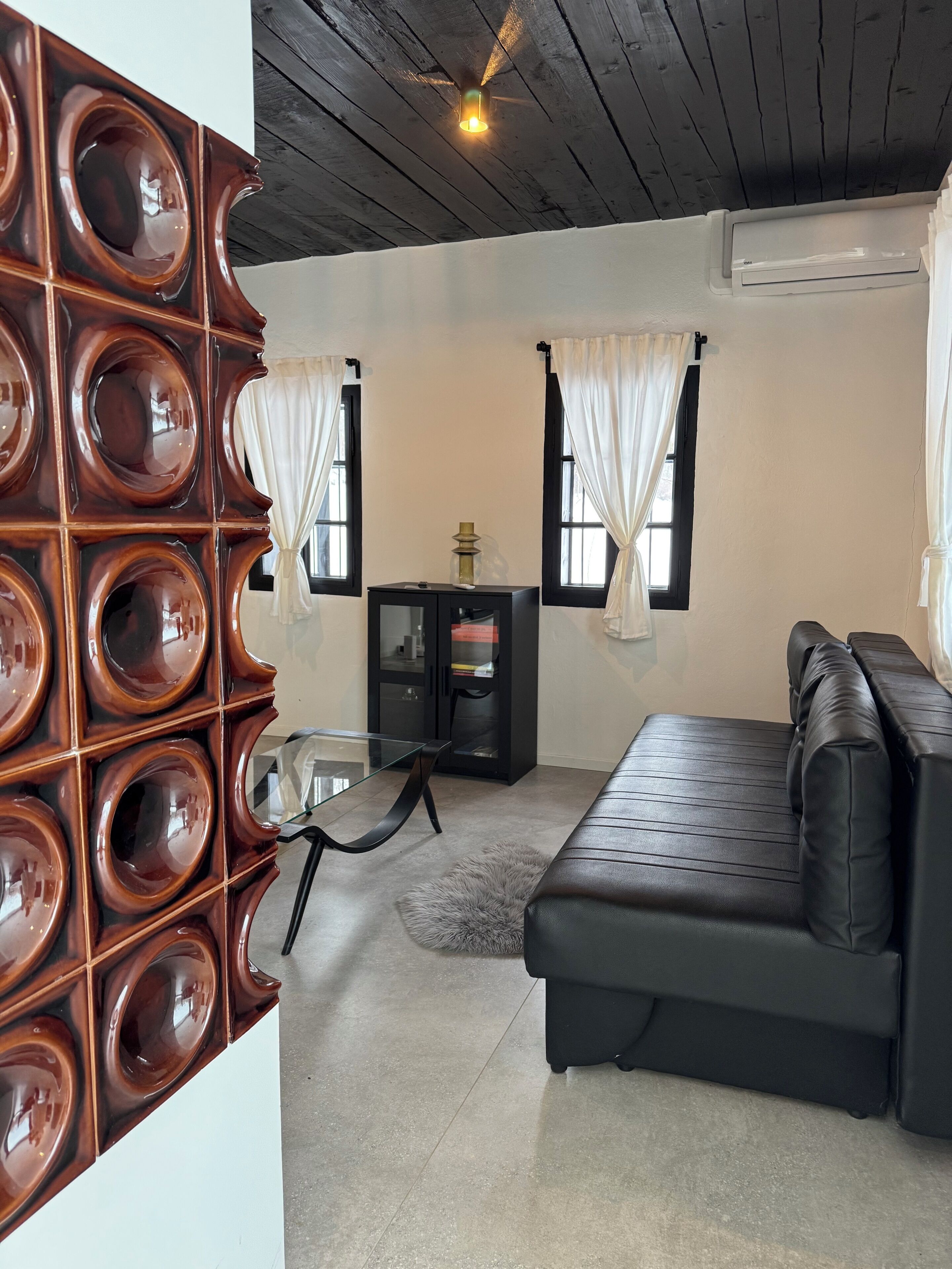 A modern living room with a glass-top dining table, a black leather sofa, and a decorative wall panel.