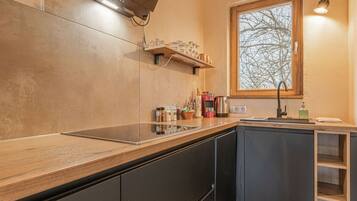 A modern kitchen with a wooden countertop, built-in cabinets, a window with a view, and a shelf with kitchenware.