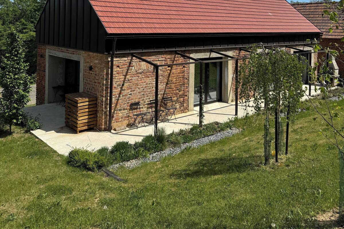 Une maison moderne avec un toit rouge, des murs en briques et un patio couvert.