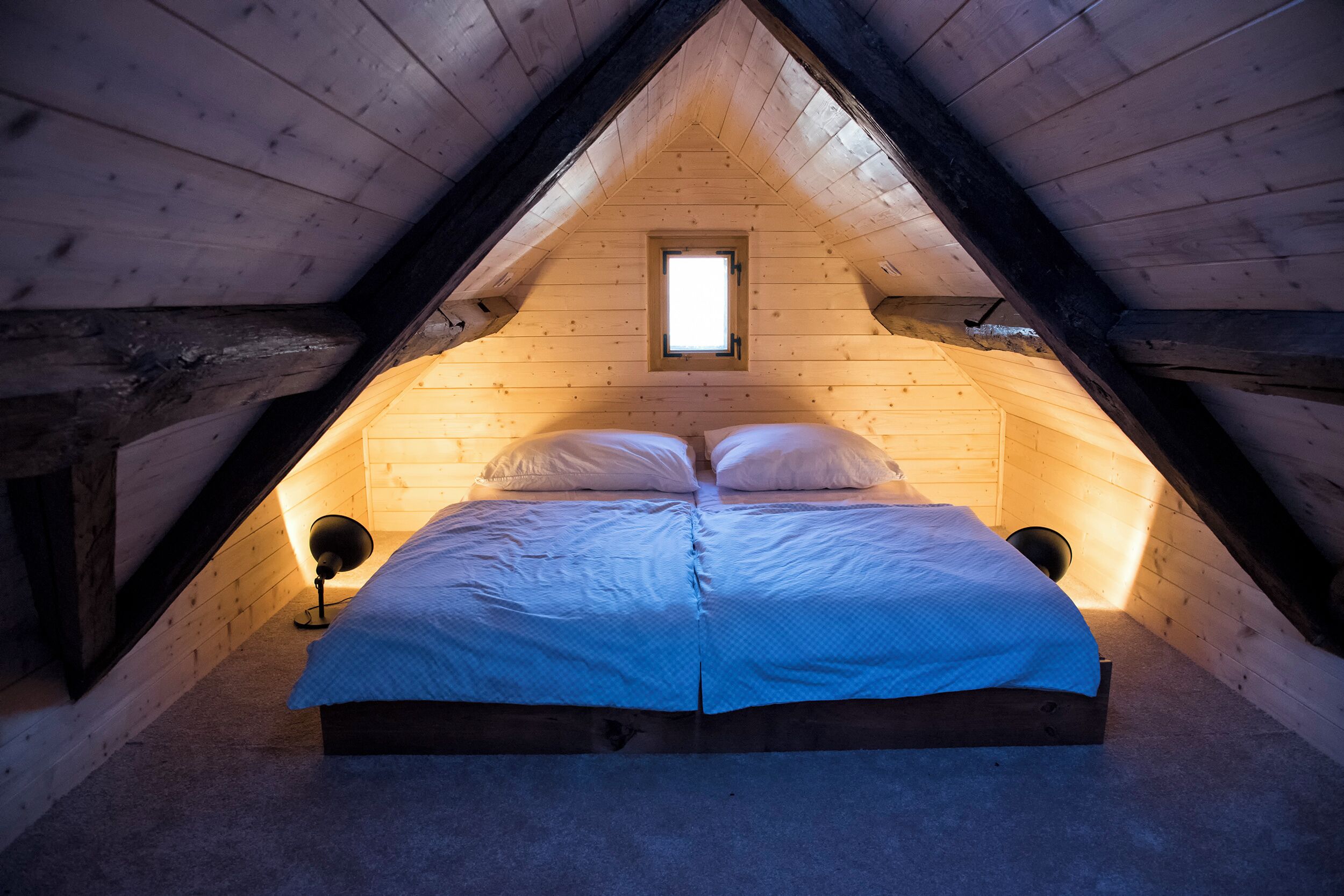 A wooden attic bedroom with a bed, a small window, and two bedside lamps.