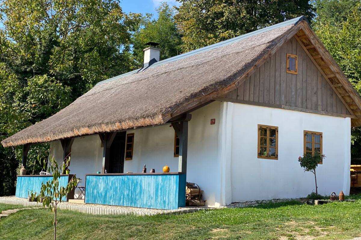 Une maison traditionnelle en bois, avec un toit de chaume, des murs blancs et une véranda bleue.