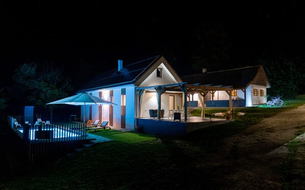 A two-story house with a covered patio and a swimming pool at night.