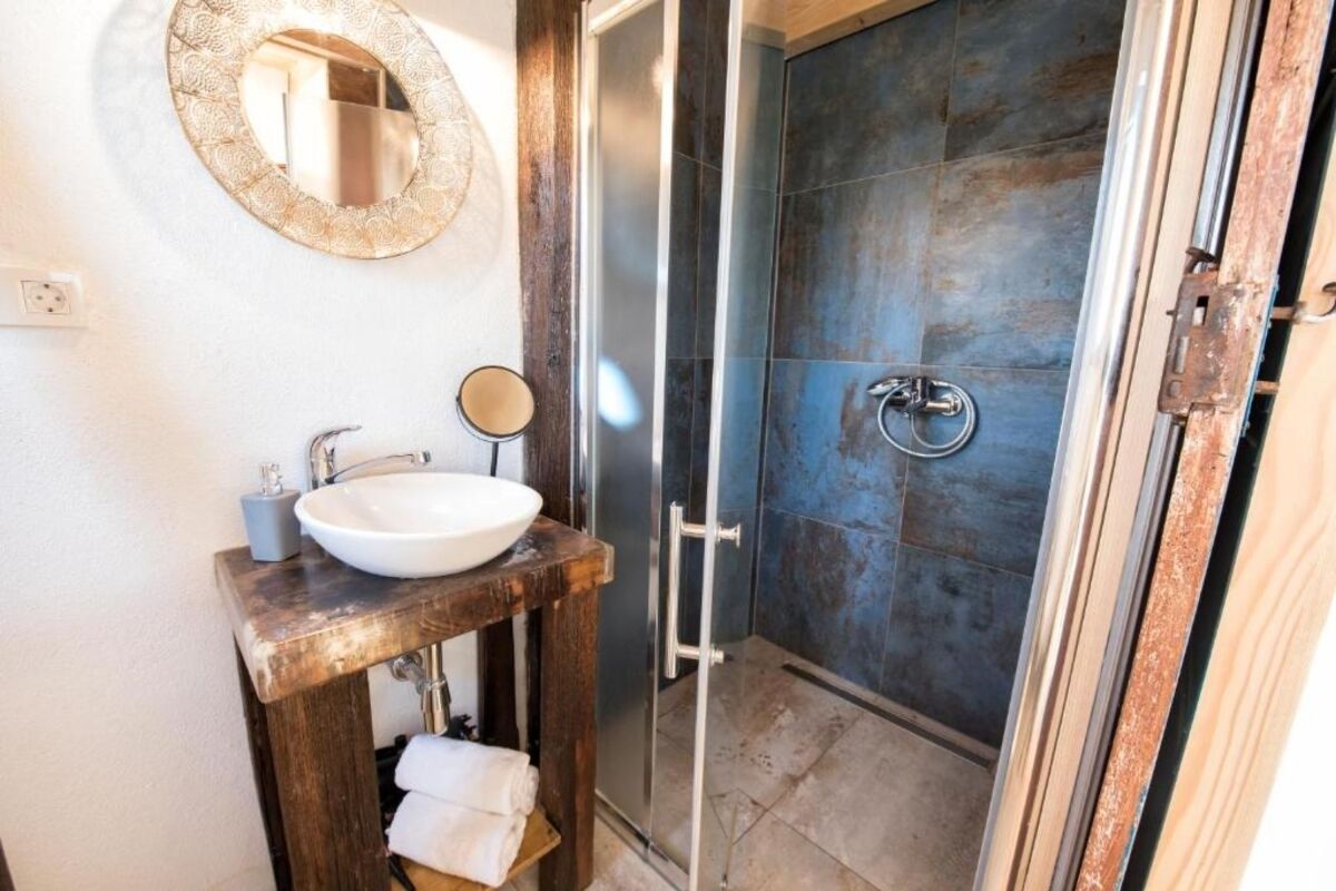 Une salle de bain avec un meuble-lavabo en bois, un lavabo blanc, un miroir rond et une cabine de douche en verre.