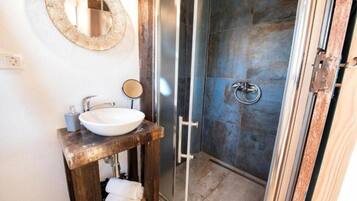 A bathroom with a wooden vanity, a white sink, a round mirror, and a glass shower enclosure.
