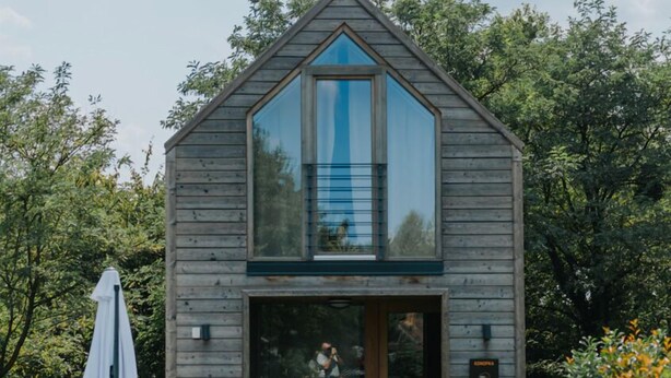 Una cabaña de madera con un amplio ventanal, una puerta de madera y un pequeño porche.