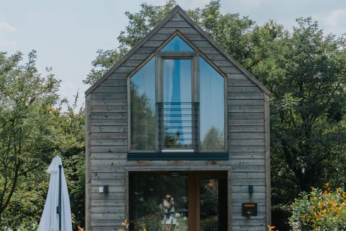 Une cabane en bois dotée d’une grande fenêtre en verre, d’une porte en bois et d’un petit porche.