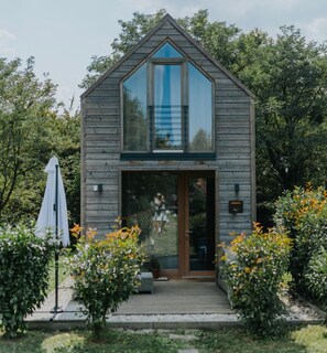 Una cabaña de madera con un amplio ventanal, una puerta de madera y un pequeño porche.