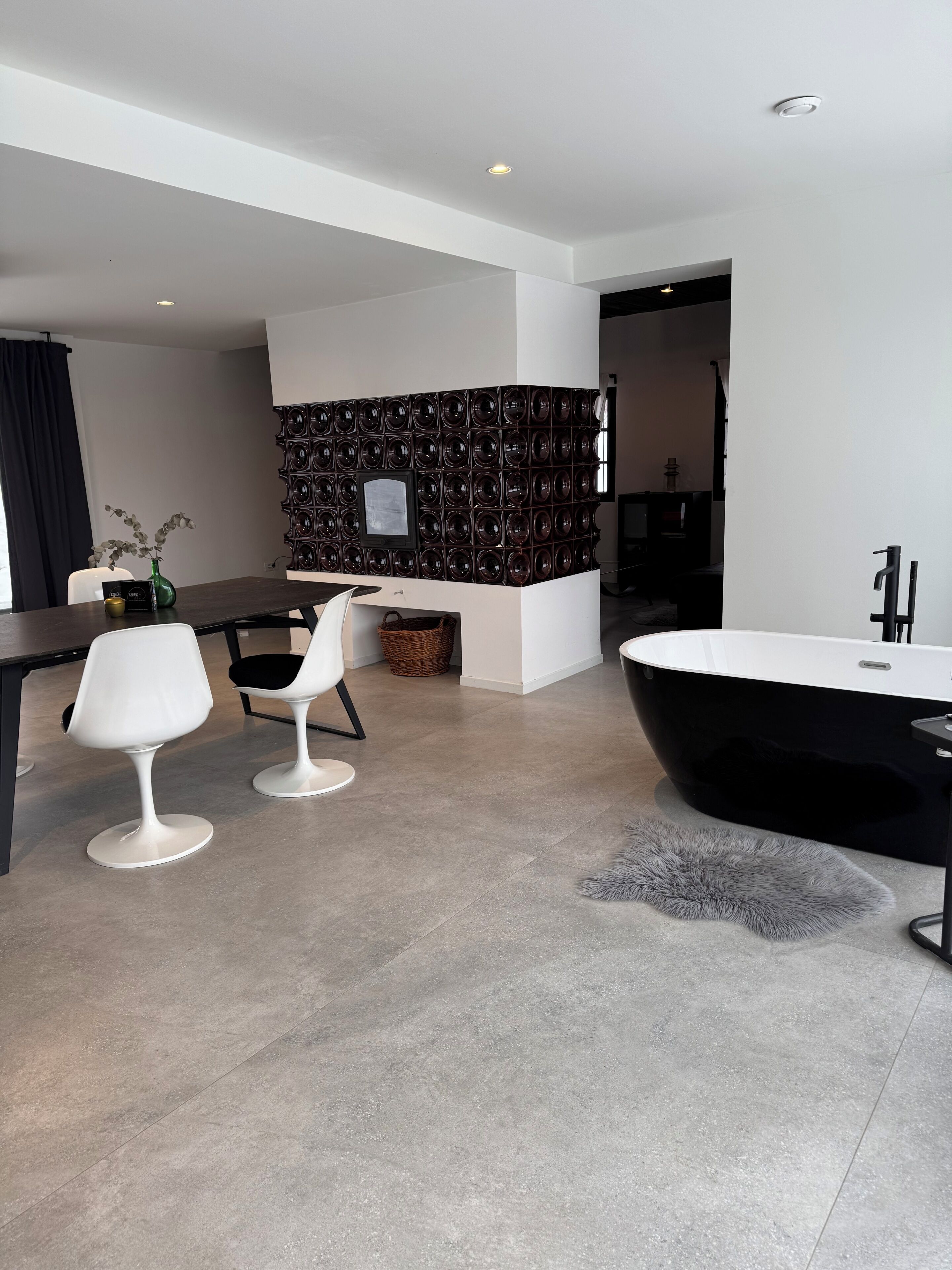 A modern interior with a black bathtub, white chairs, a dining table, and a wall with circular patterns.