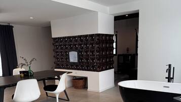 A modern interior with a black bathtub, white chairs, a dining table, and a wall with circular patterns.