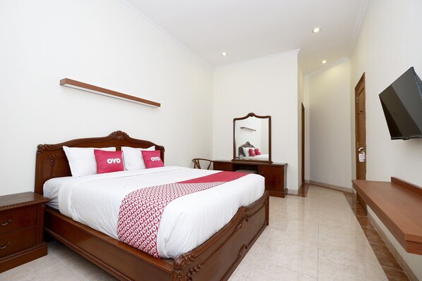 A neatly arranged bedroom with a wooden bed, a bedside table, a TV mounted on the wall, and a mirror above the dresser. - OYO 2327 Pagsis Village (Klaten)