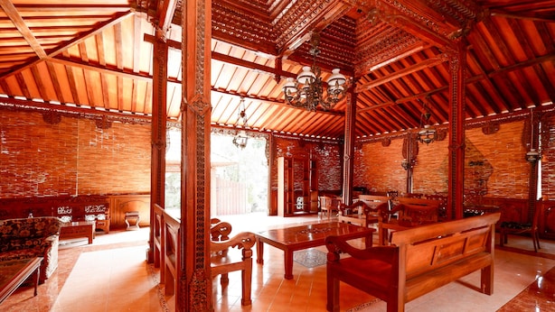 A traditional wooden interior with a high ceiling, ornate columns, and a central wooden table with benches. - OYO 2327 Pagsis Village (Klaten)