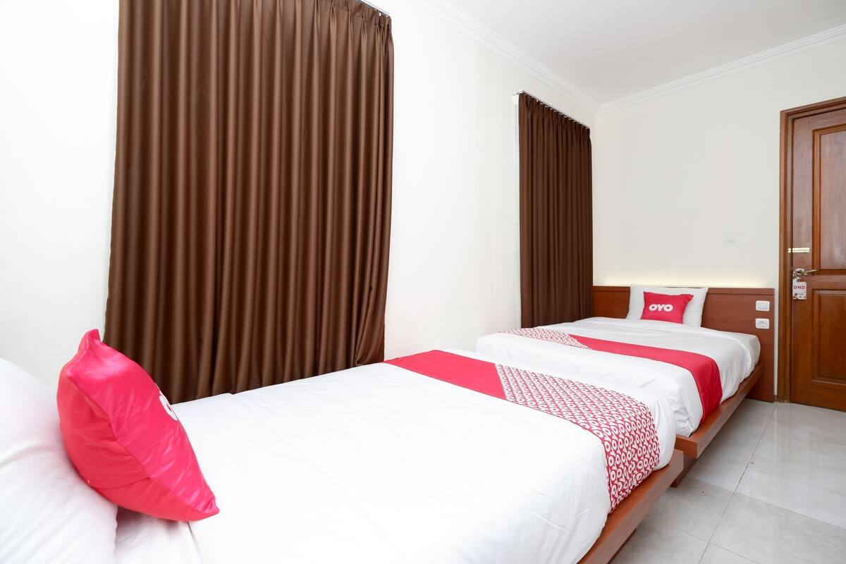A hotel room with two single beds, brown curtains, white bedding, and a wooden door.