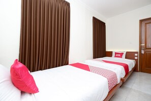 A hotel room with two single beds, brown curtains, white bedding, and a wooden door. - OYO 2327 Pagsis Village (Klaten)